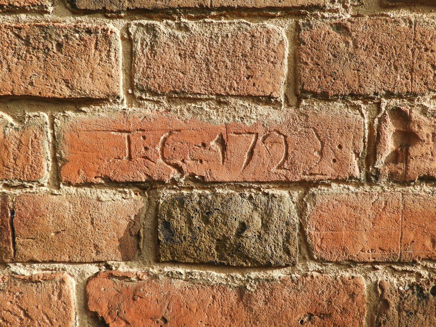 Een rode bakstenen muur met een historische inscriptie.