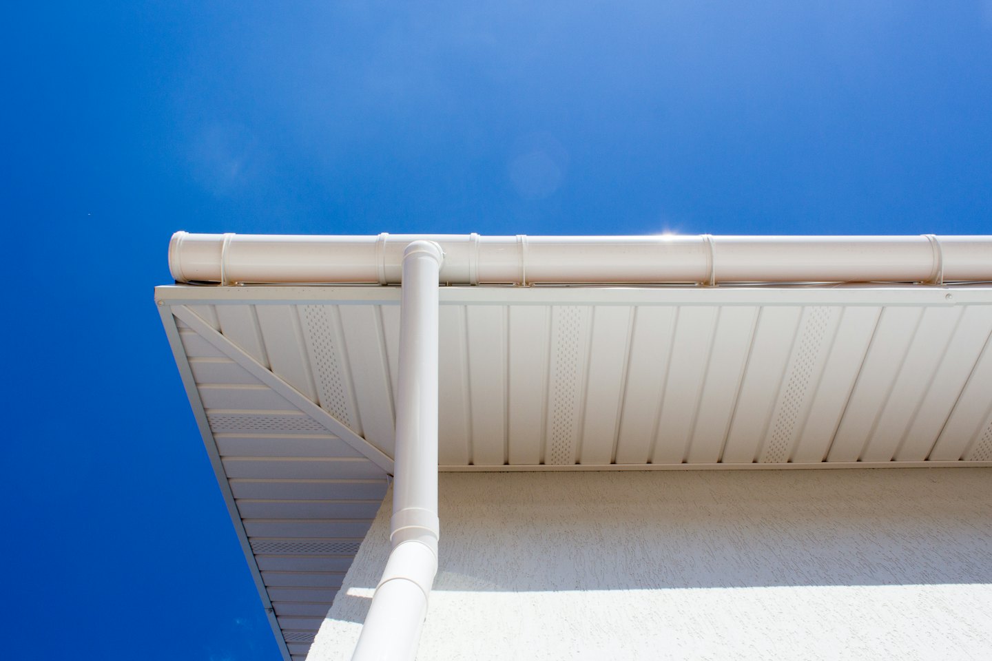 Moderne woning met witte dakgoot en regenpijp tegen een blauwe lucht.